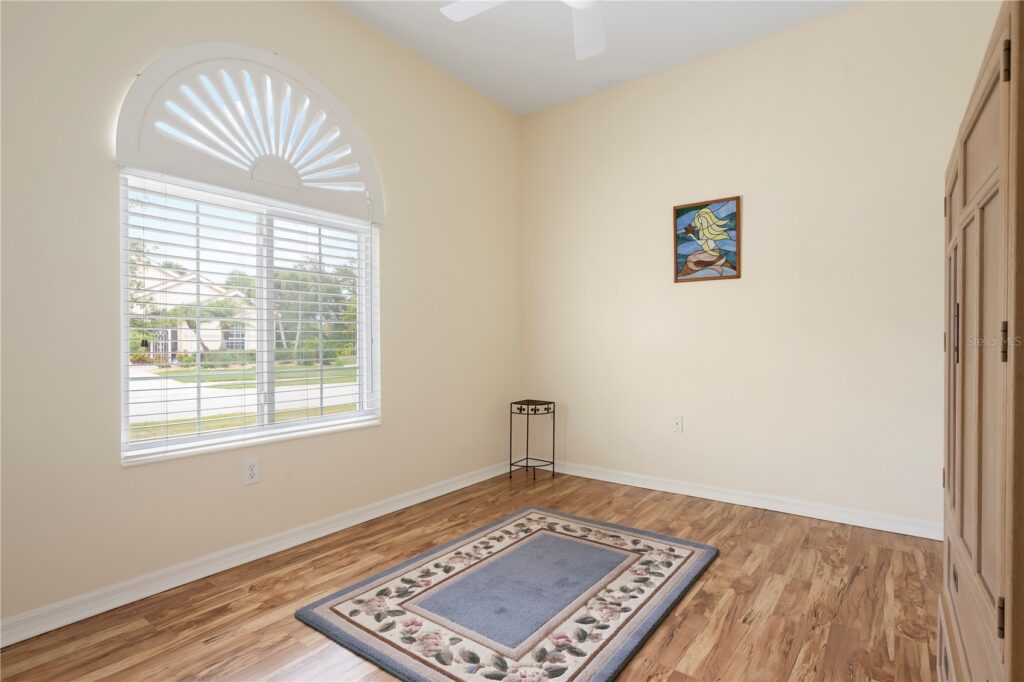 Bright empty room with wooden floor, a rug, and a window with shutters.