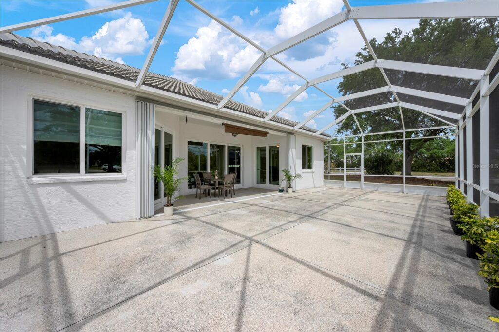 Spacious screened patio with clear roof and concrete floor under blue sky.