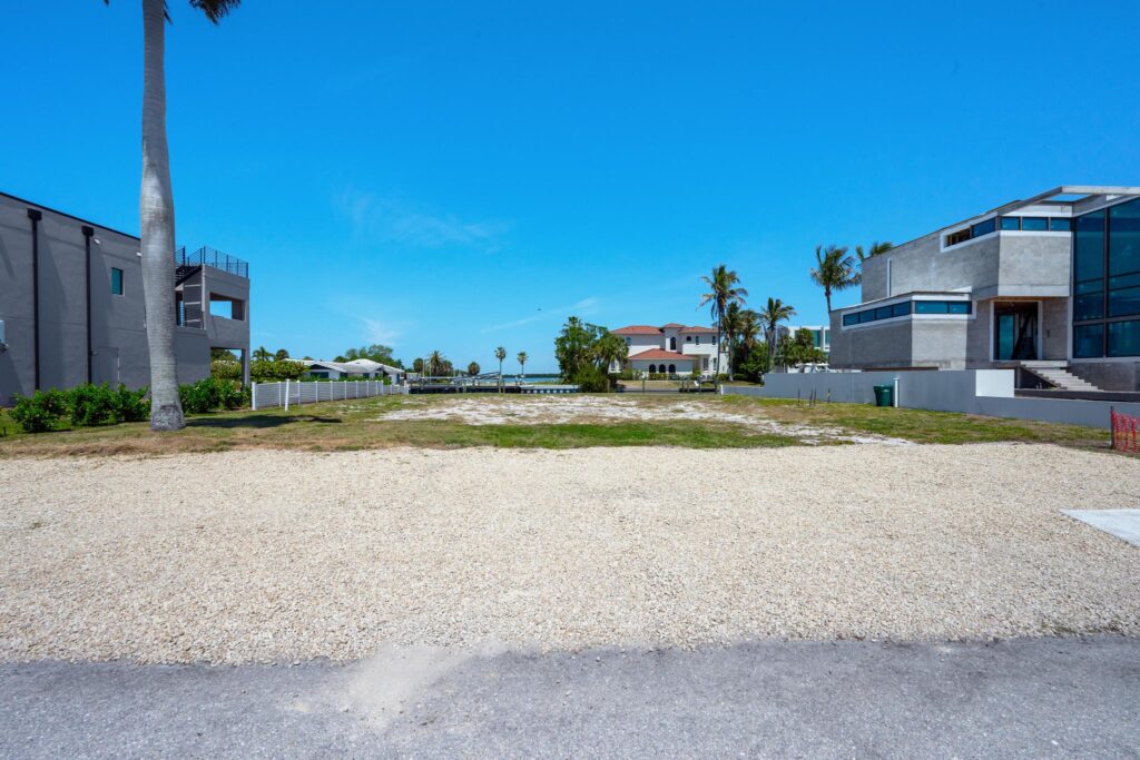 Empty gravel lot between two modern houses on a sunny day.